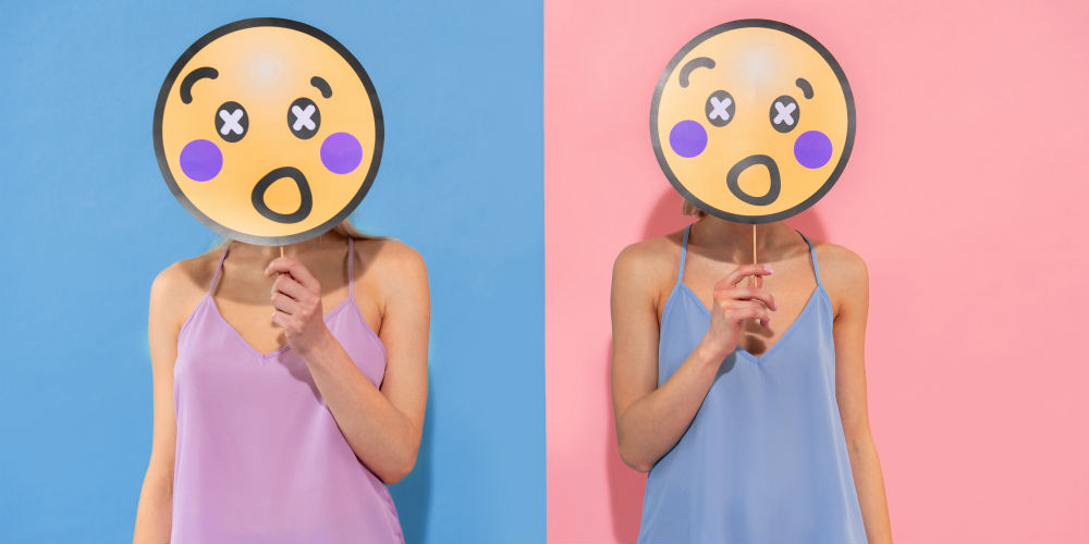 Two people standing next to each other holding emojis in front of their faces